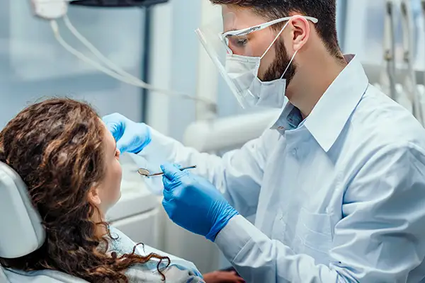 Male dentist wearing protective gear conducting an oral check up on a female patient in a modern dental clinic.